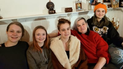 Fem kvinnor, fyra tonåringar och en vuxen, sitter i en soffa och ser glada ut.