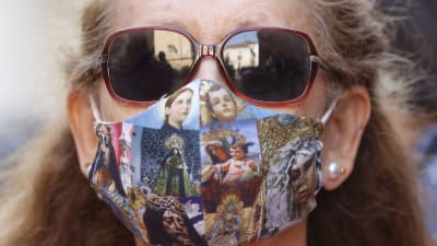 Kvinna i solglasögon bär munskydd med tryck av religiösa motiv. 
