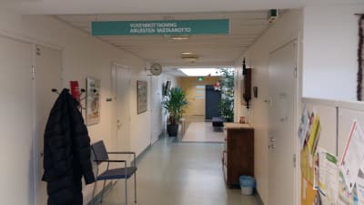 En korridor med en jacka på en hängare, en stol, en krukväxt och en skylt med texten Vuxenmottagning, på en psykiatrisk poliklinik.