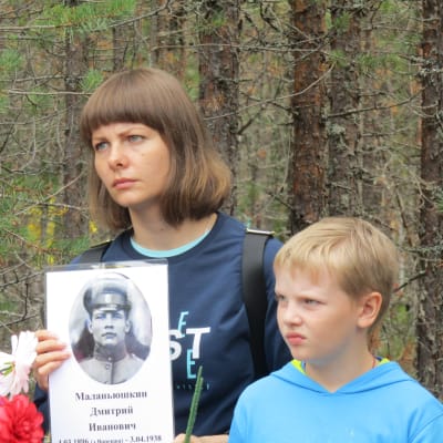 En kvinna och en pojke håller upp en bild på en soldat.