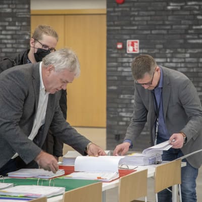 Kolme miestä kumartuneena paperien yllä allekirjoittamassa urakkasopimuksia rakennusprojektiin.