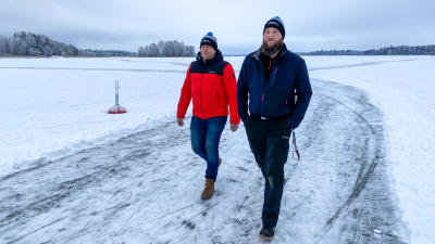 Två män i vinterkläder går över isen mot kameran.