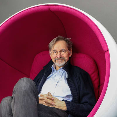 Asko Sarkola sitter i en vit-pink stol designad av Eero Aarnio.