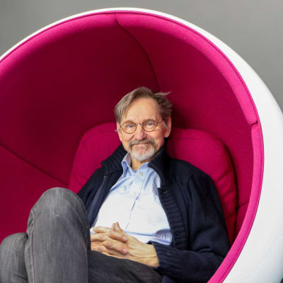 Asko Sarkola sitter i en vit-pink stol designad av Eero Aarnio.
