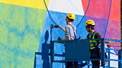 Två konstnärer målar en mural på en husvägg.