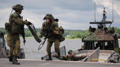 Två finska soldater kliver av en stridsbåt under en krigsövning. En chef övervakar övningen.
