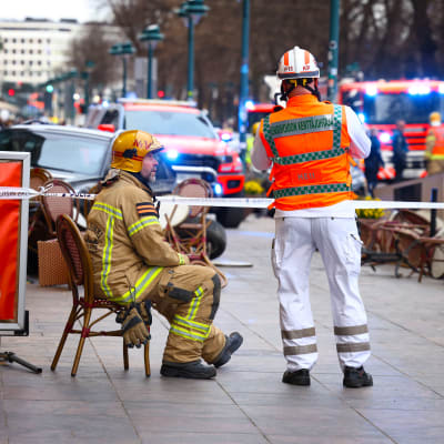 Palomies istuu tuolilla ja juttelee ensiapuhenkilöstön kanssa onnettomuuspaikalla Pohjoisesplanadilla. 