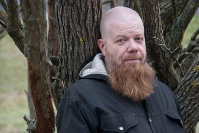 Kirjailija, runoilija, taiteilija Heikki Kännö nojaa pajupuun runkoon.