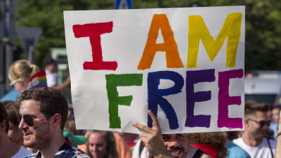 Demonstranter håller upp en skyld med texten "I AM FREE" i regnbågens färger.