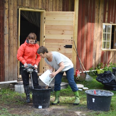 Ingrid Henriksson och Eva Godenhielm-Vuori blandar ihop massan för lerklining ute på gården.