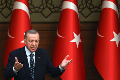 Turkiets president Recep Tayyip Erdoğan framför tre stora turkiska flaggor. 