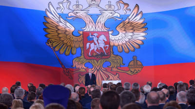 Vladimir Putin framför en enorm rysk flagga, då han höll sitt årliga linjetal den 1 mars 2018.