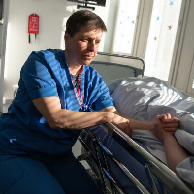 Palliatiivinen lääkäri Anu Usvasalo pitää potilasta kädestä kiinni.