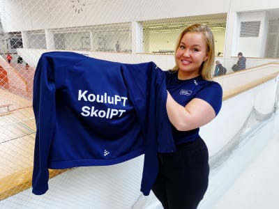 Jonna Kotivesi håller upp en collegetröja med texten skol-PT.