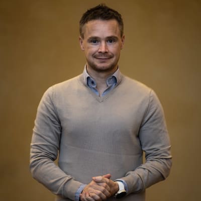 Man i grå tröja står framför gul vägg