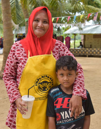Kvinna i sjal och gult förkläde håller om sin son. 