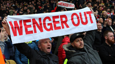 En supporter håller upp ett plakat med texten "Wenger out".