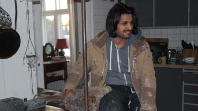 Ahmed Aljuaifari med en lurvig hund vid en gammal spis i familjen Hellgrens kök