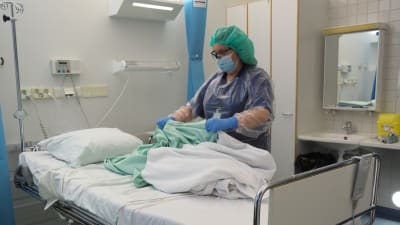 En sjukskötare byter sängkläder på en sjukhussäng.