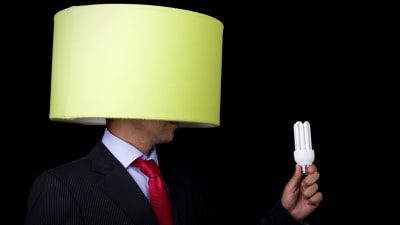 En man har en lampskärm på sitt huvud och håller i en lampa i sin hand som han håller framför skärmen.