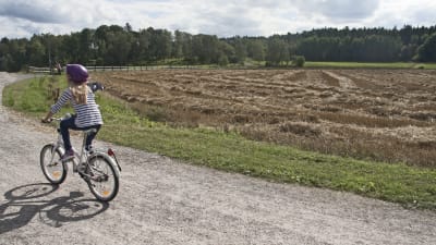 Flicka cyklar på landsväg.