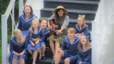 Rebecka Stretenovic på trappa medf gitarr omgiven av sjungande flickor.