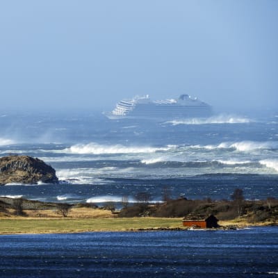 En bild på ett kryssningsfartyg i kraftig storm. I förgrunden syns land och hav.