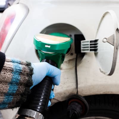 En kvinna fyller på bensin i bilens tank. 