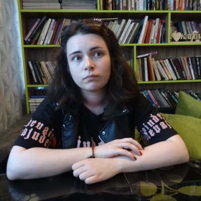 Alina Petrovitj är något så ovanligt som en rysk feminist. Här sitter hon med armarna i kors i en grön soffa framför en bokhylla.