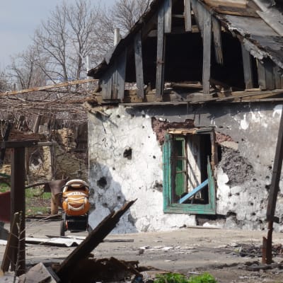 Ett sönderbombat hus, på gården plåt och trävirke men också en orange barnvagn