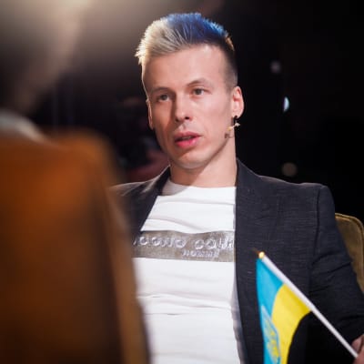 Antti Kurhinen istuu nojatuolissa ja heiluttaa Ukrainan lippua.