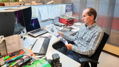 En man sitter vid ett skrivbord i ett kontor och tittar på ett papper.
