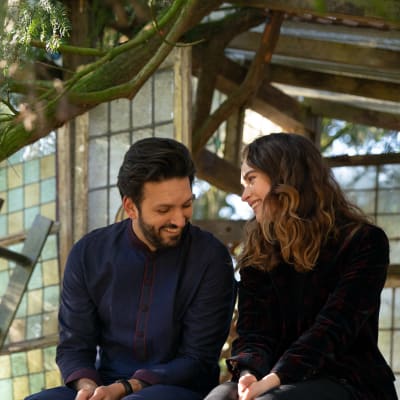 Den indiska mannen Kaz och den brittiska kvinnan Zoe sitter och tittar på varandra i en träkoja.