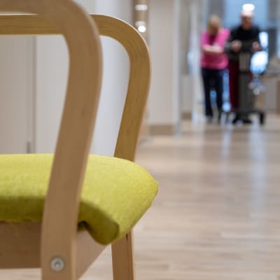 Fysioterapeutti avustaa vanhusta kävelyharjoituksessa Myyrmäen vanhustenkeskuksessa. Etualalla kuvassa tuoli.