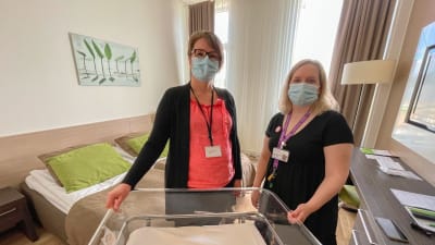 Kaksi naista seisoo Taysin potilashotellissa ja katsoo kameraan. Naisten edessä vauvan sänky.