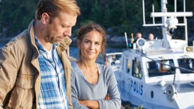 Karaktärerna Thomas och Nora på en brygga med en polisbåt i bakgrunden.