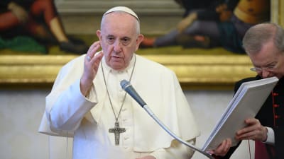 En äldre man i vit dräkt och vit huvudbonad samt ett stort metallkors på bröstet. Påven Franciskus i Vatikanen den 17 juni 2020.