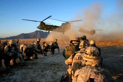 Soldater på knä väntar på att transporthelikoptrar ska landa, berg i bakgrunden, damm stiger när helikoptrarna landar.