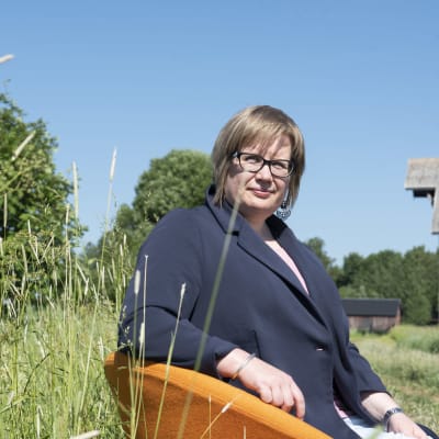 Ympäristöministeriön erityisasiantuntija Maaret Väänänen istuu oranssilla tuolilla keskellä vehreää peltomaisemaa.