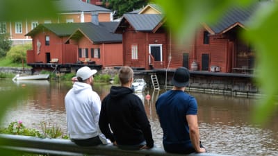 De tre pojkarna sitter med ryggen mot och tiitar ut över Borgå å och strandbodarna.
