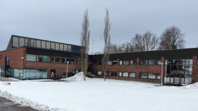 Ett mörkrött tegelhus med många fönster. Visar innergården som är täckt med snö. Det är kommunhuset i Ingå.