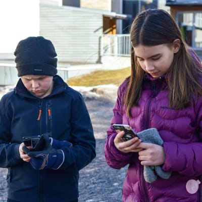 Två skolbarn tummar på sina telefoner.