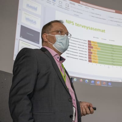 Ilkka Pirskanen håller en presentation. Power point med staplar i bakgrunden.