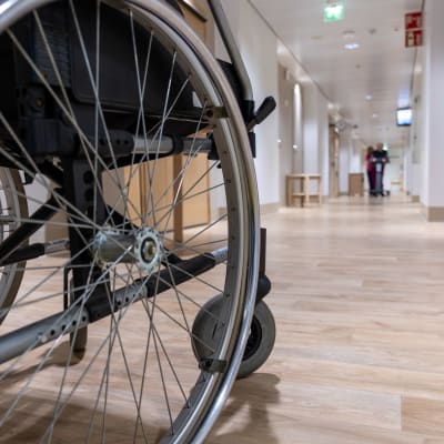 Ett rullstolshjul i förgrunden, i bakgrunden en lång korridor.