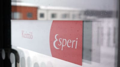 En skylt av Esperi Care på en glasdörr, i glasdörren speglas Attendos vårdhem som står granne med Esperi i Kimito.
