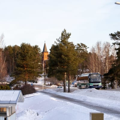 Linja-auto kulkee Miehikkälän kylänraitilla talvella, taustalla näkyy Miehikkälän kirkon torni