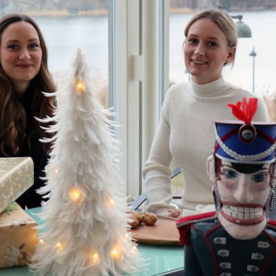 Pähkinänsärkijä-baletin fanit Emma ja Peppi Larjamo istuvat Kansallisoopperan lämpiössä. Kuvan etualalla Pähkinänsärkijä-nukke, jota käytetään myös esityksessä.