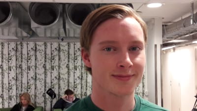 Daniel, i närbild, grön tröja, tapeter med björkar i bakgrunden, skolans aula.