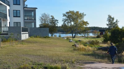 En människa går på en bergssluttning. I bakgrunden syns spåren av en tidigare gångstig. På höger sida syns bostadshus.