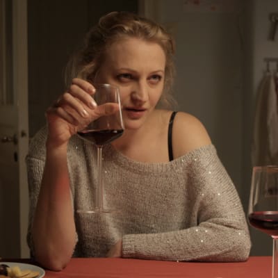 Exfrun sitter vid ett köksbord med ett rödvinsglas i handen.
